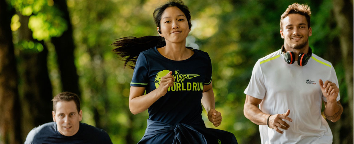 Kolme Wings for Life World Run -juoksutapahtuman osallistujaa juoksemassa iloisena Philips-urheilukuulokkeet p&auml;&auml;ss&auml;.